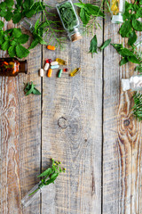 Homeopathy. Leaves of healing herbs, bottles and pills on wooden background top view copyspace