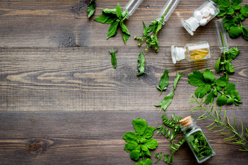 Homeopathy. Leaves of healing herbs, bottles and pills on wooden background top view copyspace