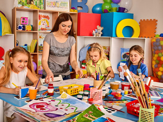 Fototapeta premium Kids playroom organization of children painting and drawing in kid's club. Craft lesson in primary school. Kindergarten teacher and students work together. Preparing for a children's art exhibition.