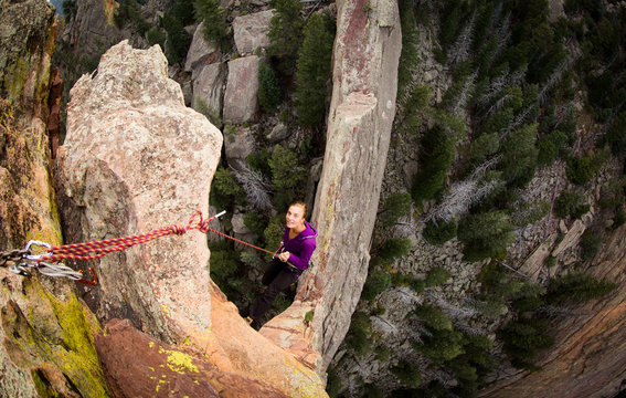 Young Adult Woman Rappels off exposed rock on the Maiden in Colorado