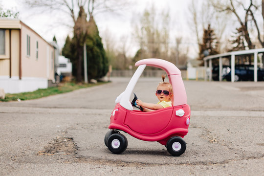 Toddler girl with pink sunglasses in pink toy car
