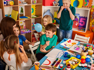 Small students girl and boy painting in art school class. Children drawing by paints on table. Male kid shows his drawing in kindergarten. Many children draw together. Children indulge.