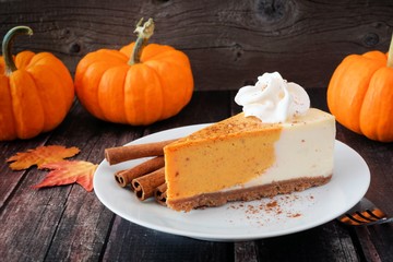 Slice of pumpkin cheesecake with whipped cream on a dark rustic wood background - obrazy, fototapety, plakaty