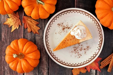 Slice of pumpkin cheesecake with whipped cream, overhead table scene on a rustic wood background
