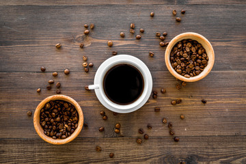 Cup of black coffee near coffee beans on wooden background top view
