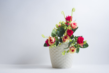 Beautiful artificial rose flowers stand in a plastic pot on a white background;
