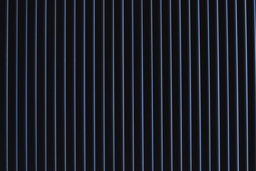 Obraz premium Even thin stripes with a blue tint on a black background. The light passes through the closed shutters at dawn.