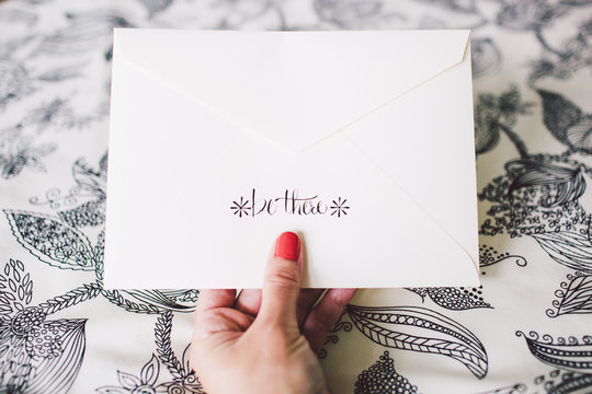 A hand holding an invitation envelope with hand lettering that readsbe there " hand hold" hand holding """ hand holding an invitation e"