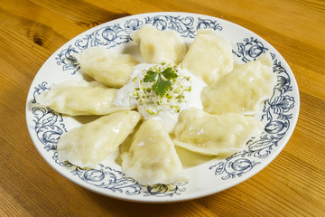 Cooked dumplings with cheese pork scratching and creme fraiche on wooden table.