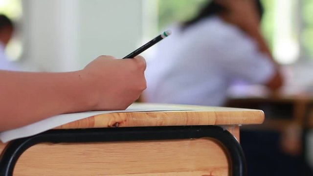 Asian Students holding pencil in hand doing multiple-choice quizzes or testing exams answer sheets exercises on old wood table In secondary school, college university classroom in education concept