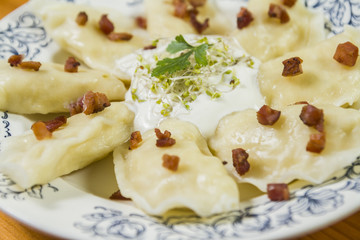 Cooked dumplings with cheese pork scratching and creme fraiche on wooden table.