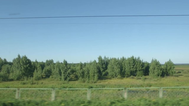 POV: High-speed Train moves past a low forest, green fields and a lake in a sunny day