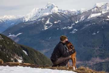 Man embraces the dog that's licking his face after a hike to the summit. Picture taken on top of...