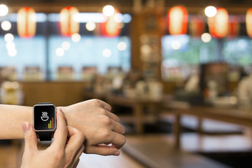 Smart watch on hand with ordering app on the screen over a wooden table in japanese restaurant
