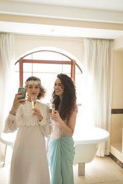 Bride and bridesmaid taking selfie while having champagne