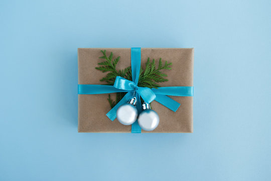 Gift box wrapped of craft paper, blue ribbon and decorated fir branches and silver Christmas balls on the blue background, top view. Christmas present.