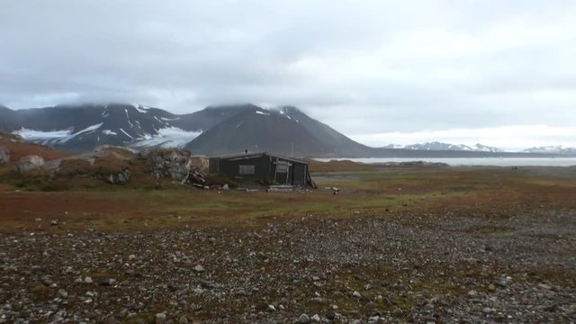 Old house on desert coast of Arctic Ocean on background of mountains. Wildlife in Nordic badlands. Unique footage and natural landscape of Spitsbergen.