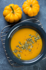 Dark grey plate of pumpkin soup topped with pumpkin seeds and spices, flat-lay