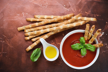 Above view of gazpacho cream-soup with grissini and fresh green basil on a rusty metal background, studio shot
