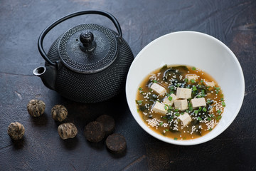White bowl with miso soup, asian teapot and green tea balls, selective focus