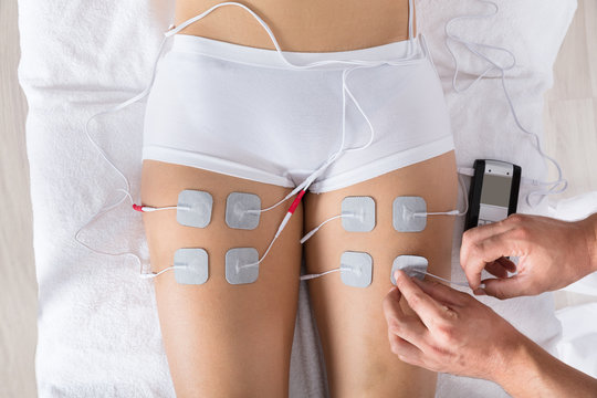 Therapist Giving Electrodes Therapy On Woman's Thigh