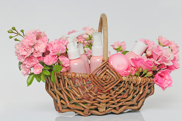 Fototapeta na wymiar rose based cosmetics. set of cosmetic products in pink bottles and jars and pink roses in a brown wicker basket . Organic Cosmetics Concept