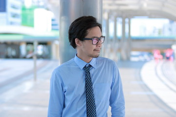 Portrait of confident young Asian business man leaning a pole at outside office.