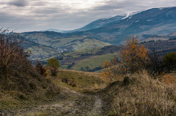 dirt road through mountainous countryside. beautiful late autumn scenery with snowy tops of high mountain ridge in a distance