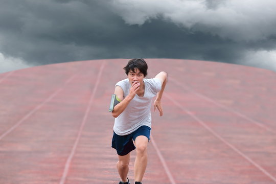 Young Asian runner running on track with weather storm on dark cloudy sky background.