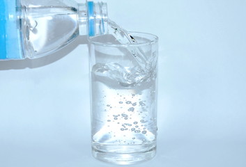 water pouring from bottle in drinking glass on white background
