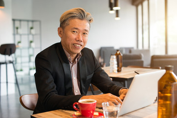 asian senior male using laptop on cafe