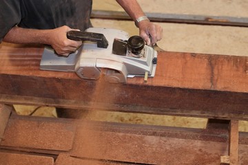 Aerial view of senior carpenter using electric planer on a piece of wood in carpentry workshop. Selective focus and shallow depth of field.