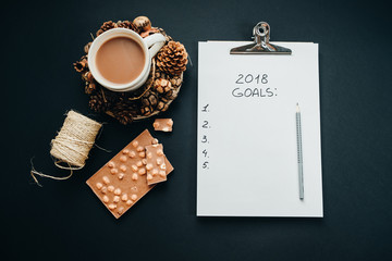 2018 goals list with pencil, chocolate, cocoa, cone on black background, top view, flat lay