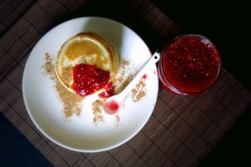 Homemade sweet pancakes with raspberries jam on a black background.