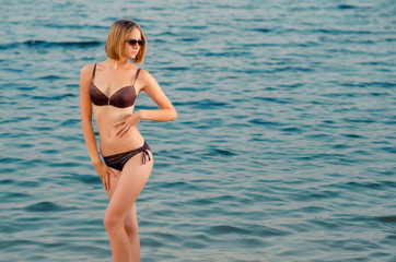 Beautiful  caucasian young woman in a glasses on the beach, is standing on azure water
