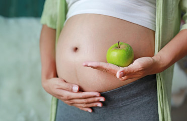 Pregnant woman holding Green Apple fruit at her tummy.