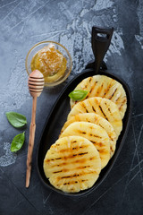 Frying pan with grilled pineapple slices and honey, high angle view on a dark gray stone background