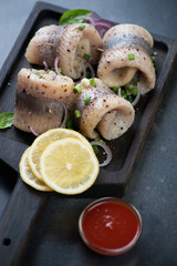 Black wooden serving tray with herring fillet rolls, selective focus