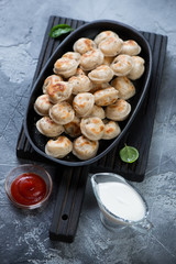 Metal plate with roasted pelmeni on a black wooden serving board, studio shot