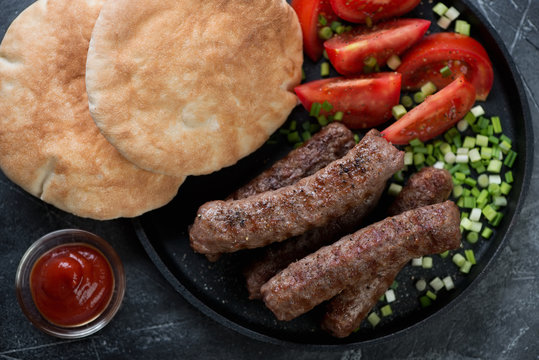 Above view of barbecued balkan cevapcici or skinless beef sausages served with green onion, tomatoes and pita bread