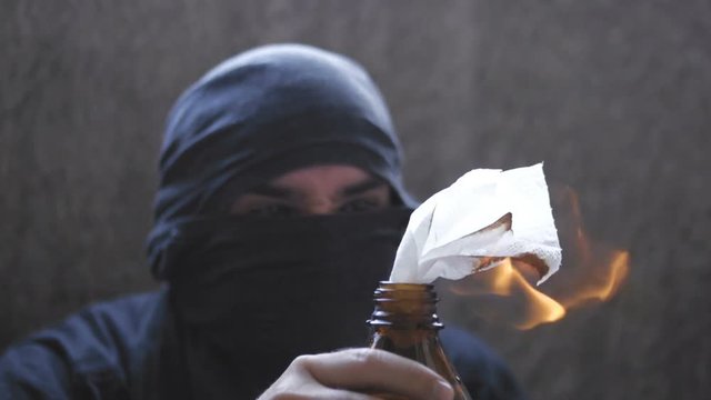 Black bloc anarchist is lighting the molotov cocktail and holding in hand