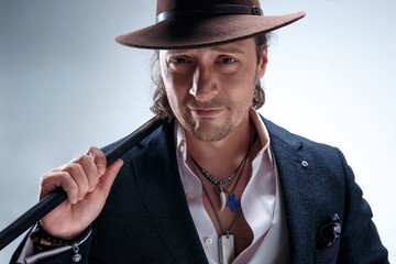 The mature man in a suit and hat holding cane.