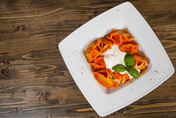 Ravioli topped with tomato sauce,with cheese and the fresh basil on white plate. on a wooden background. with copy space. top view