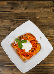 Ravioli topped with tomato sauce,with cheese and the fresh basil on white plate. on a wooden background. with copy space. top view