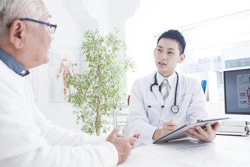 A young doctor is talking to an old man in a consultation room