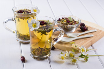 Herbal tea ingredients with hip roses, chamomile, herbs on white wooden table