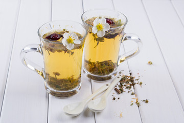 Two cups of herbal tea with rosehip , chamomile, herbs on  white wooden table