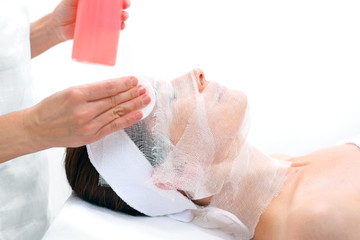 Pielęgnacja skóry twarzy w gabinecie kosmetycznym. Kosmetyczka nakłada preparat na twarz kobiety.