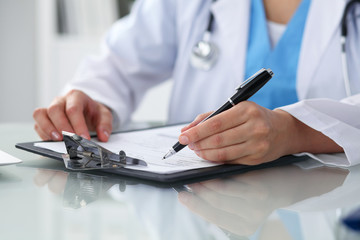 Fototapeta premium Doctor woman filling up medical form while sitting at the table, close-up of hands