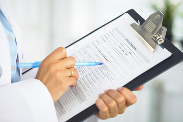 Close-up of a female doctor filling  up medical form at clipboard while standing straight in hospital